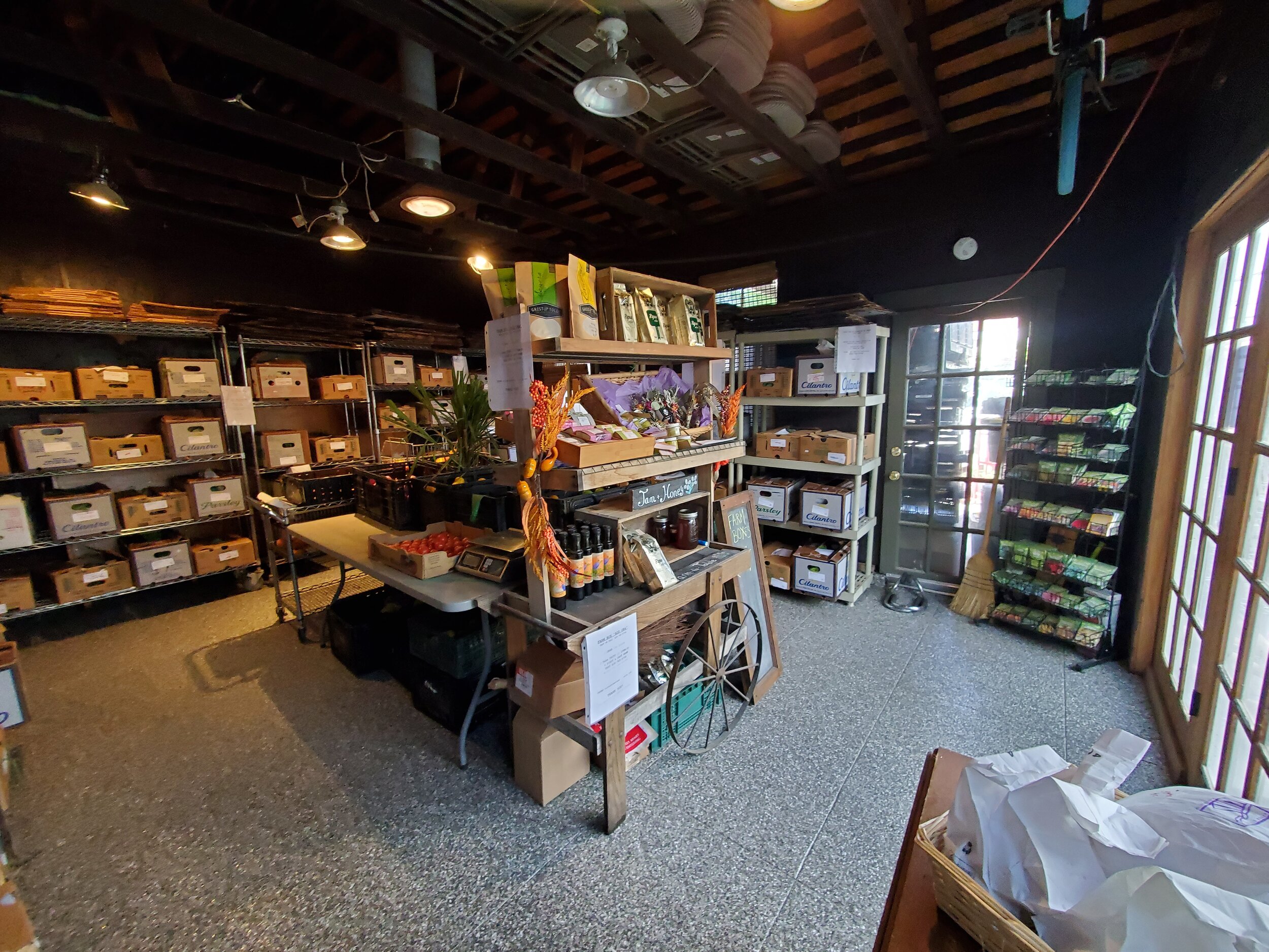 Interior view of a cozy retail space featuring shelves stocked with various boxes, plants, and organic products. A central table displays items for sale, while a door leads to the outside. The warm lighting and rustic decor create an inviting atmosphere for shoppers.