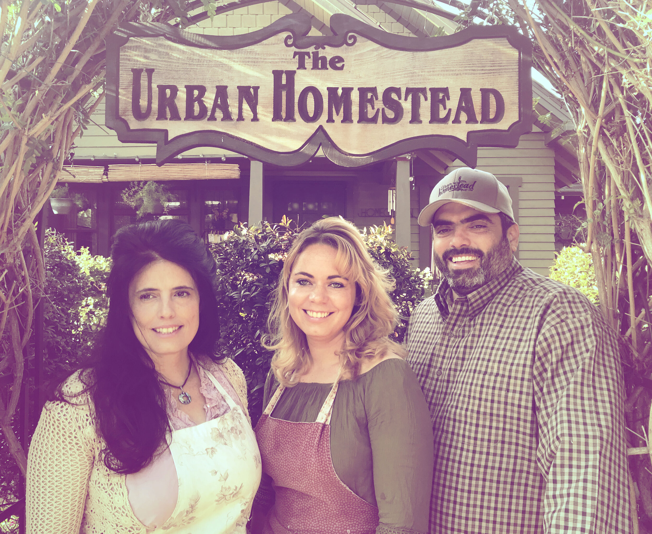 Group of three smiling individuals in front of The Urban Homestead sign, showcasing a welcoming atmosphere for urban gardening and sustainable living.