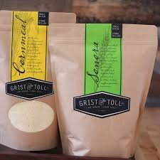 Dervaes+Institute+-+gristandtoll Two bags of Grist & Toll flour, one labeled "Cornmeal" in yellow and the other "Senora" in green, displayed on a wooden surface. The packaging features a rustic design, emphasizing quality and artisanal milling.