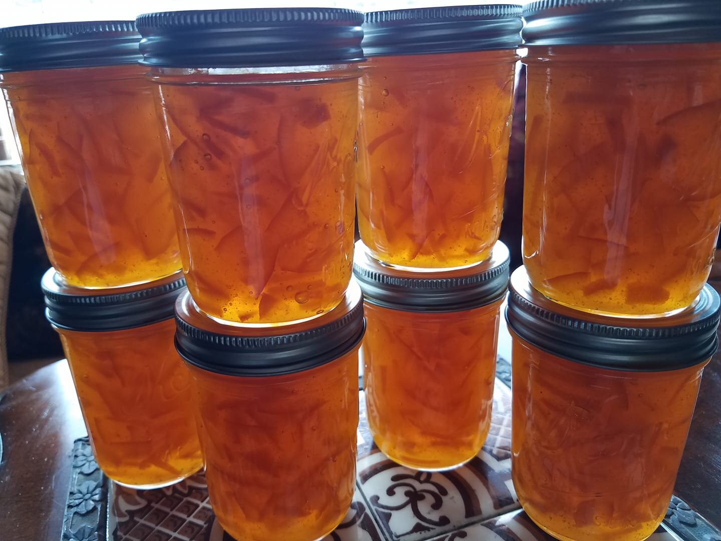Dervaes+Institute+-+marmalade Jars of homemade fruit preserves filled with vibrant orange jelly and thin slices of fruit, arranged neatly on a wooden table. The jars feature metal lids and showcase the rich color and texture of the preserves, highlighting a successful canning process.